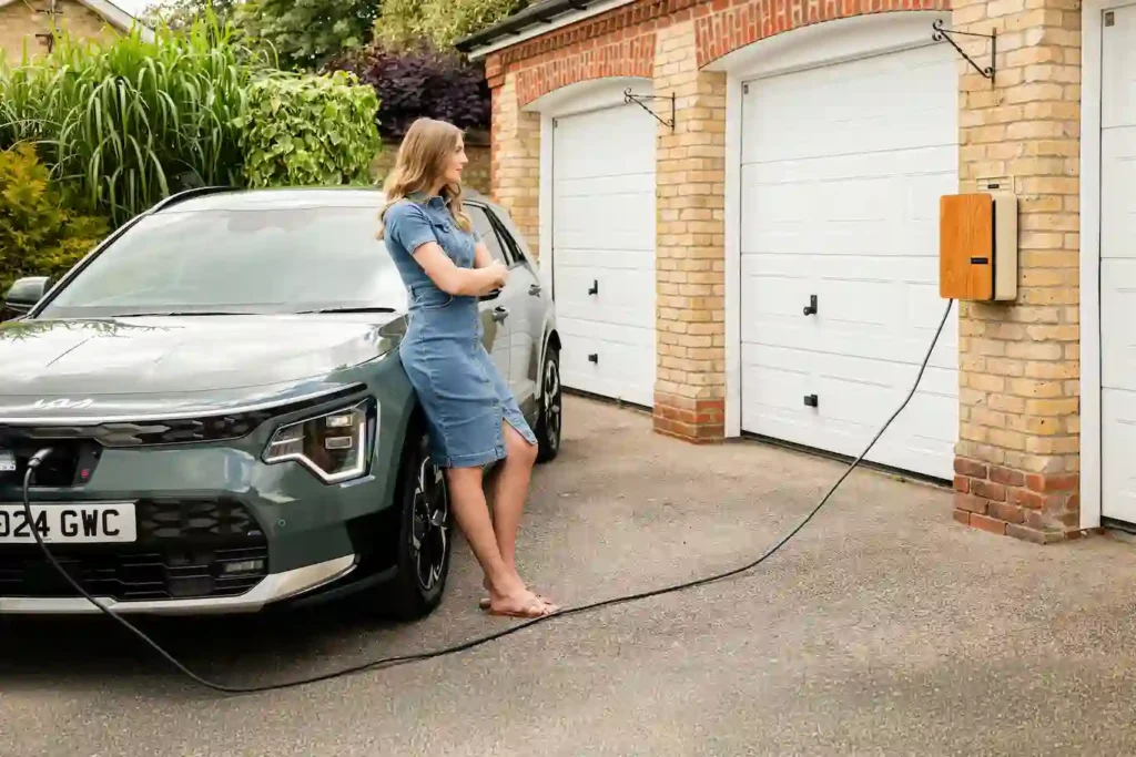 Femme devant son garage rechargeant sa voiture éléctrique